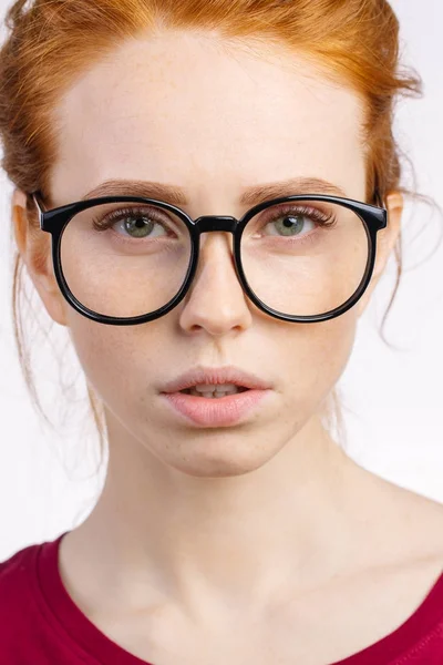 Rothaarige Frau mit Brille mit Haarknoten blickt in die Kamera auf weißem Hintergrund — Stockfoto