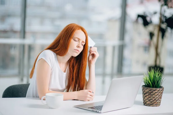 Pensando mujer de negocios sentado en la mesa con el ordenador portátil, la celebración de la tarjeta de crédito vacía — Foto de Stock