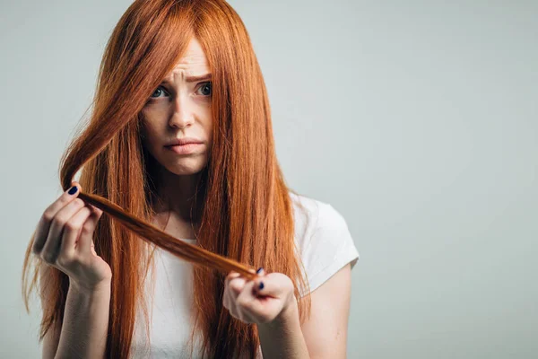 Sad redhead girl holding her damaged hair looking at camera. — Stock Photo, Image