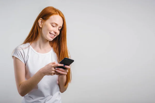 Портрет улыбающейся рыжей женщины, держащей смартфон и смс — стоковое фото