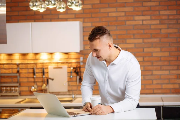 Man aan het werk thuis op een project, zitten aan witte tafel kijken naar laptop — Stockfoto