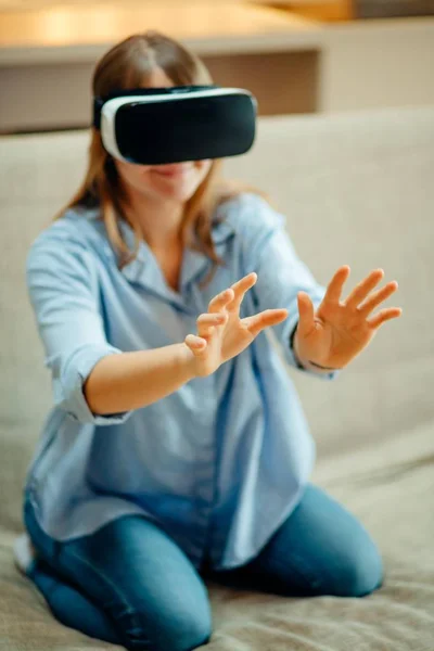 Mujer ajustando sus auriculares VR y sonriendo mientras está sentada en la alfombra en casa — Foto de Stock