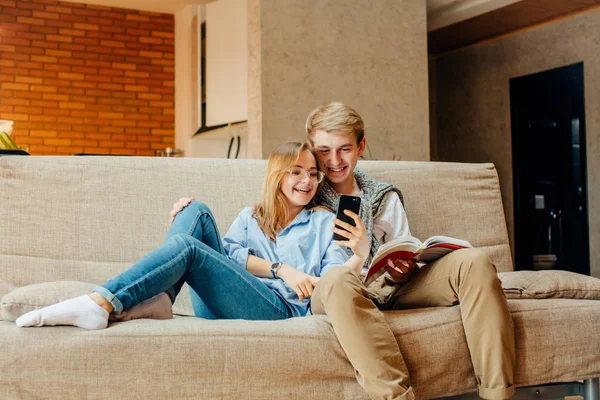 Pareja sentada en el sofá, ocio juntos, libro de lectura de hombre, mujer usando el teléfono — Foto de Stock