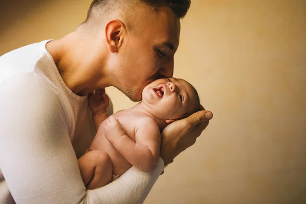 Отец держит новорожденного ребенка и целует его у окна — стоковое фото