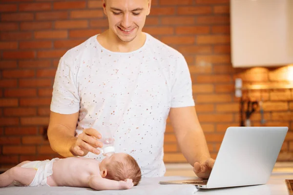 Dad trying to work while standing with his newborn babe in home office interior — Stock Photo, Image