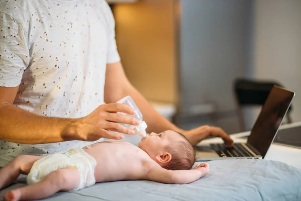Pai tentando trabalhar enquanto de pé com seu bebê recém-nascido em casa escritório interior — Fotografia de Stock
