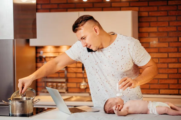 dad trying to work on laptop and talk on phone with his newborn babe in home