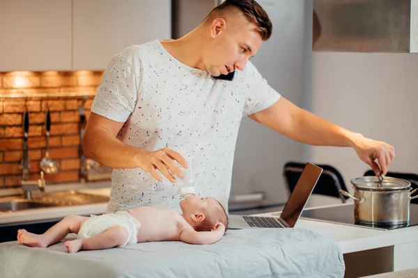 Single dad working on laptop computer at home while taking care of his baby son — Stock Photo, Image