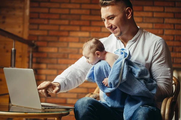 Отец с новорожденным ребенком работает из дома с помощью ноутбука — стоковое фото