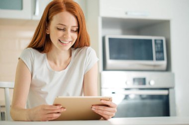 Masanın üzerinde evde dijital tablet kullanarak çalışan mutlu kadın