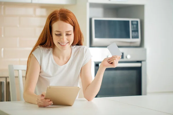 Woman online shopping using tablet and credit card in kitchen — Stock Photo, Image