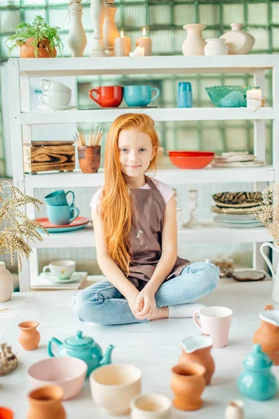 Mädchen mit vielen Tassen aus Ton sitzt im Töpferatelier — Stockfoto