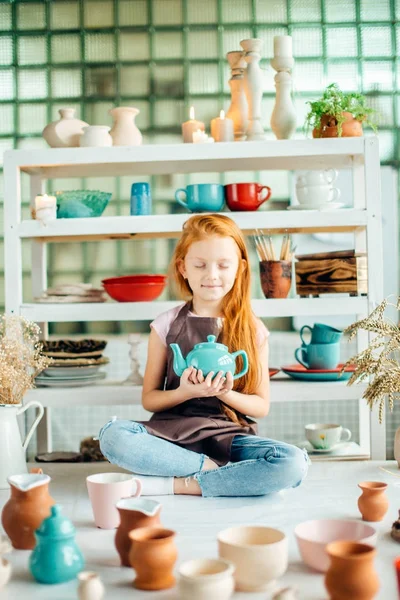 多くのカップを持つ粘土ワーク ショップ スタジオで座っている赤毛の女の子 — ストック写真