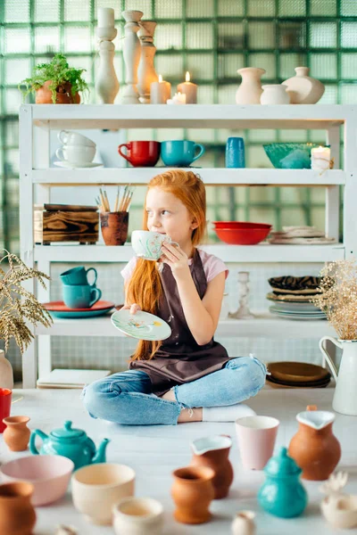 Rödhårig flicka sitter på lera verkstad studio med många kopp — Stockfoto