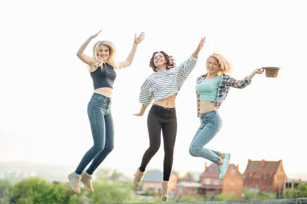 Three happy joyful young women jumping and laughing together at park — Stock Photo, Image