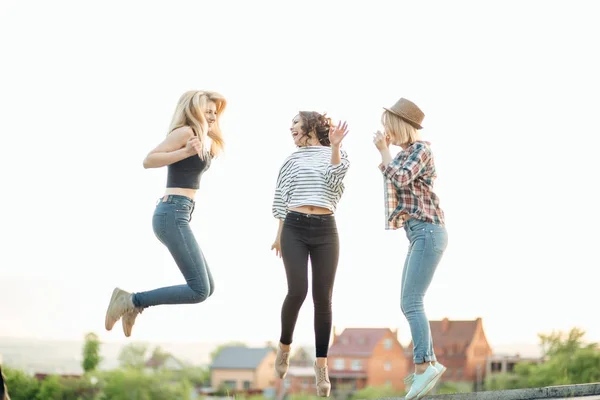 Tres felices mujeres jóvenes alegres saltando y riendo juntos en el parque —  Fotos de Stock
