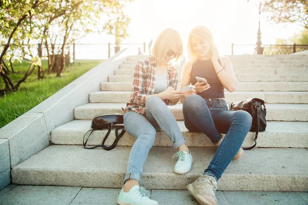 Két gyönyörű diák nézi a média elégedett-ra vonal-ban szúró telefon-ban park — Stock Fotó