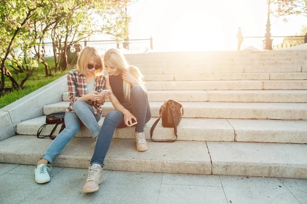 Két gyönyörű diák nézi a média elégedett-ra vonal-ban szúró telefon-ban park — Stock Fotó