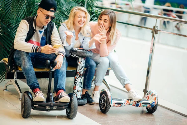 Group of people on electric scooter hoverboard sitting at bench and using phone — Stock Photo, Image