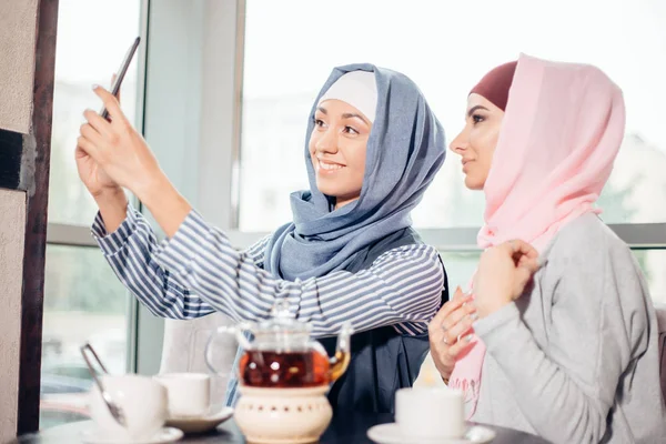 Iki mutlu genç Müslüman kadını kabul kendi kendine portre ile handphone café'de — Stok fotoğraf