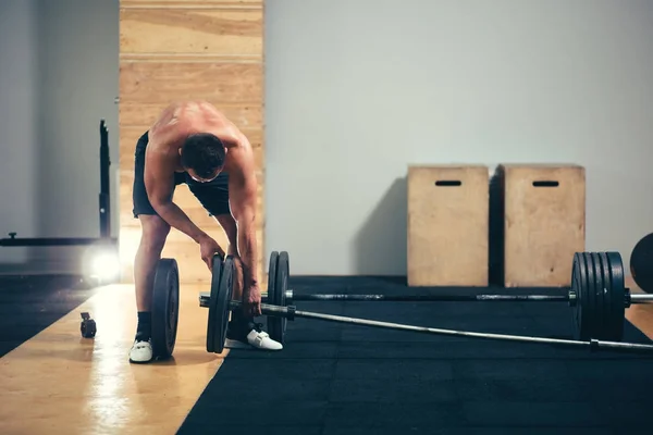 Mann bereitet sich auf Übungen mit Langhantel im Fitnessstudio vor, hält Langhantelplatte in den Händen — Stockfoto