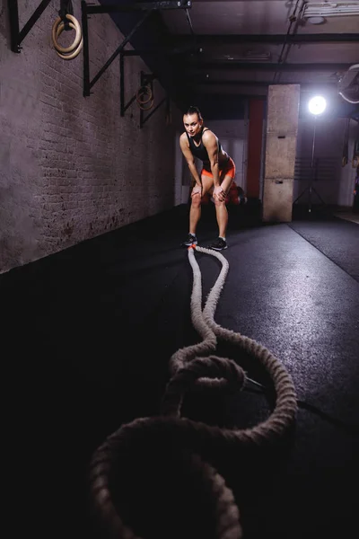 Deportista de pie en el gimnasio después de su entrenamiento de cuerda de batalla y mirando hacia abajo — Foto de Stock