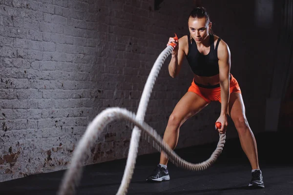 Battle ropes session. Attractive young fit and toned sportswoman training in gym