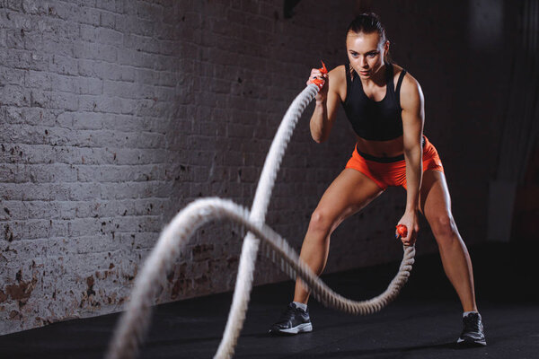 Battle ropes session. Attractive young fit and toned sportswoman training in gym