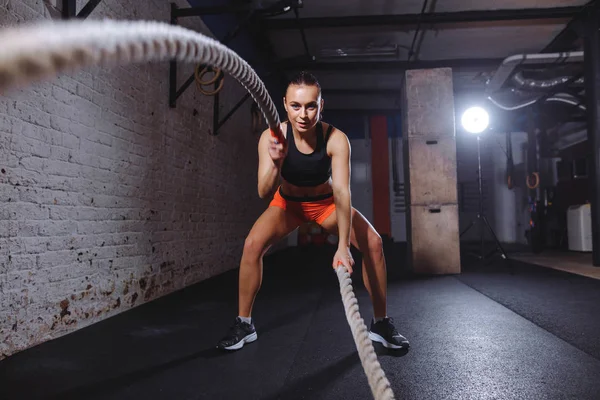 Attractive young fit and toned sportswoman working out with battle ropes — Stock Photo, Image