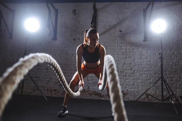 Jovem mulher trabalhando com cordas de batalha em cross fit ginásio — Fotografia de Stock