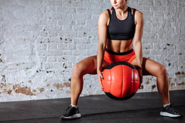 Atractiva mujer con pantalones rojos y top negro posando con balón de medicina — Foto de Stock