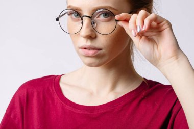 Kızıl saçlı gülümseyen kadın kırmızı gömlek giymiş beyaz arka plan üzerinde gözlük tutun