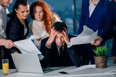 Elleri meslektaşları belgeleri ile çevrili olan kafa tutan işadamı