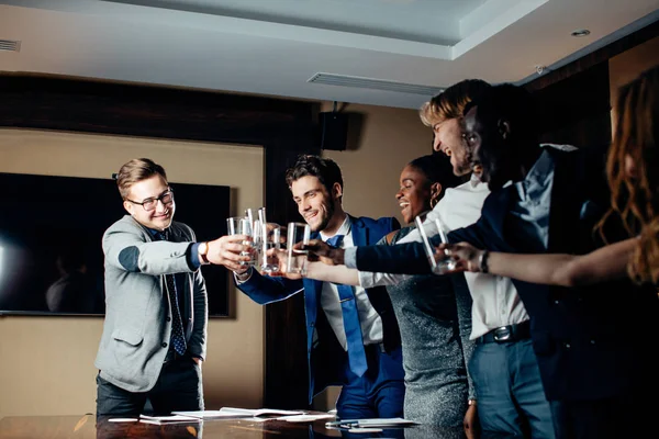 Gente de negocios tintineando gafas y sonriendo mientras celebran en la reunión — Foto de Stock