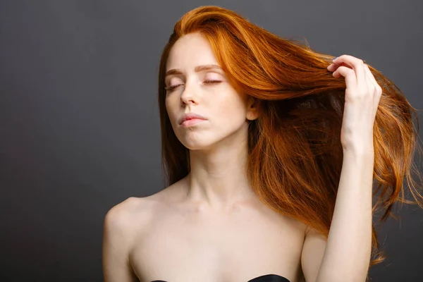 Mulher ruiva segurando seu cabelo saudável e brilhante, cinza estúdio — Fotografia de Stock