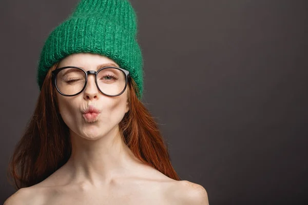 Рыжая женщина в очках и зеленой шляпе надувает губы, готовясь к поцелую — стоковое фото