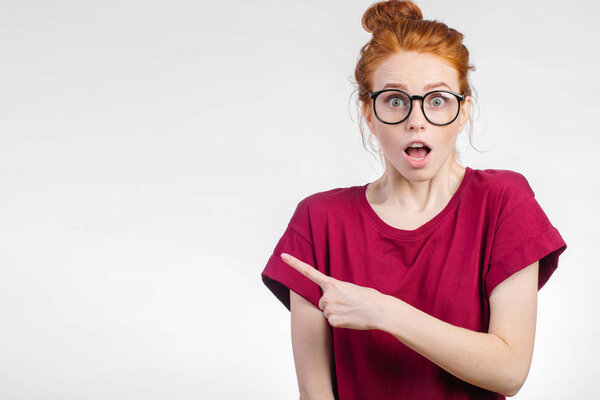 Surprised girl showing empty copy space with her finger white background