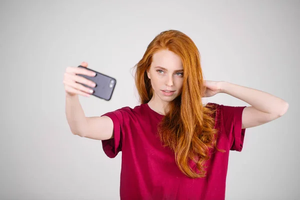Rousse fille prend un selfie. Elle a de longs cheveux roux. porte un t-shirt marsala — Photo