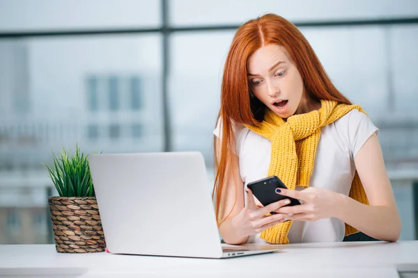 Chica pelirroja feliz enviar un mensaje SMS a un amigo mientras trabaja en la oficina moderna — Foto de Stock