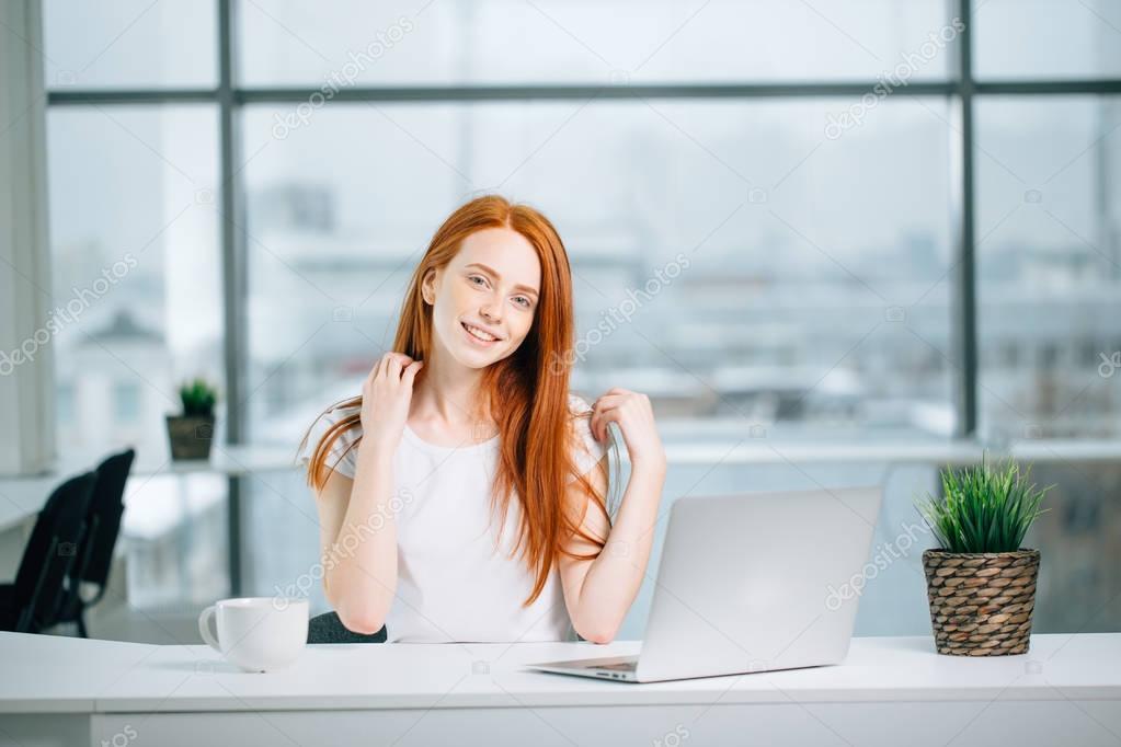 beautiful redhead girl works at laptop and looking at camera