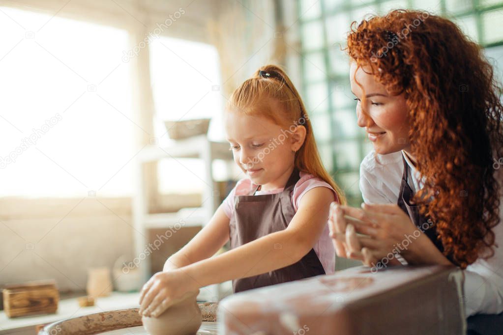redhead mother and her child daughter moulding with clay on pottery wheel