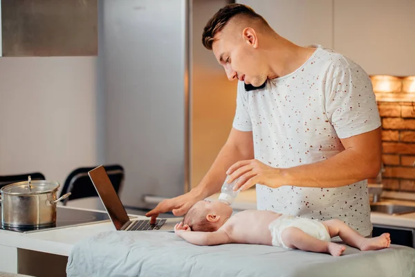 Pai alimentando seu bebê ao tentar trabalhar no laptop — Fotografia de Stock