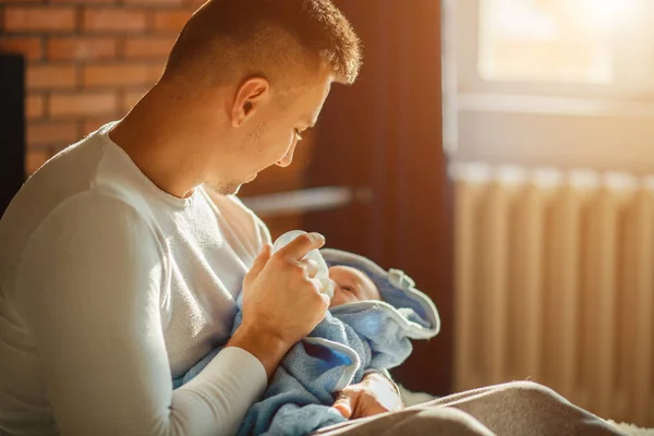 Šťastný otec krmení svého novorozeného syna s mlékem v posteli doma — Stock fotografie