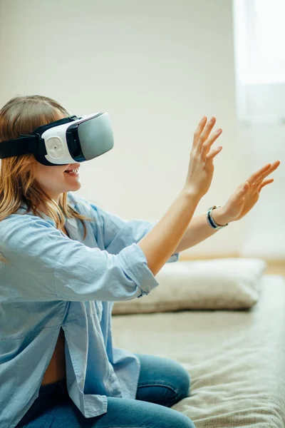 Mujer ajustando sus auriculares VR y sonriendo mientras está sentada en la alfombra en casa — Foto de Stock