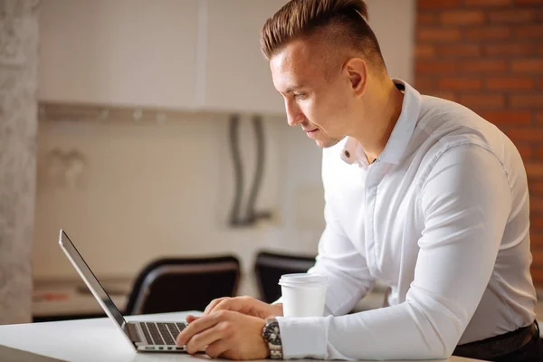 Man aan het werk thuis op een project, zitten aan witte tafel kijken naar laptop — Stockfoto