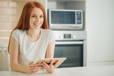 Tablet tutarak ve kameraya bakarak mutlu genç kadın