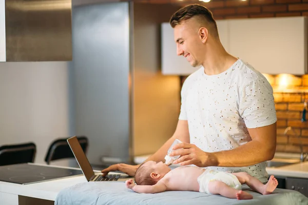 dad trying to work while standing with his newborn babe in home office interior