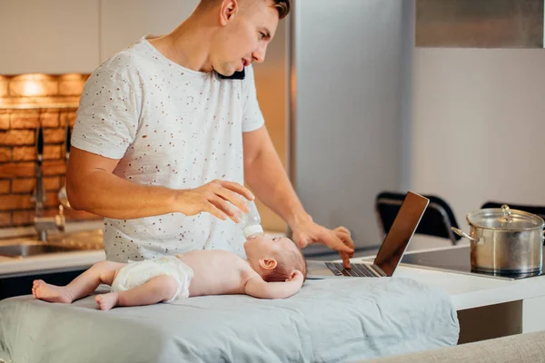 dad trying to work on laptop and talk on phone with his newborn babe in home
