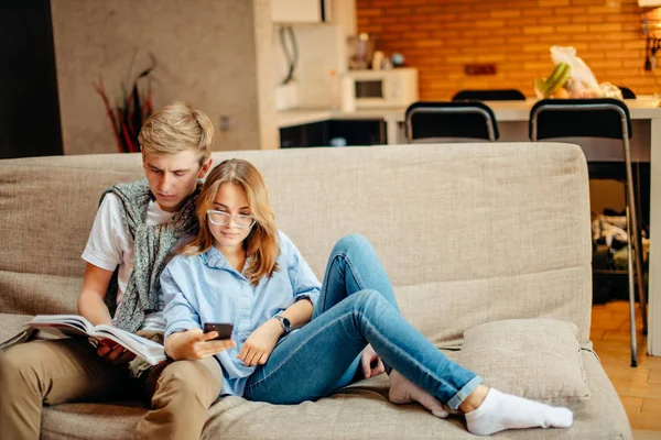 Paar zittend op de Bank, vrije tijd samen, leesboek voor man, vrouw met behulp van de telefoon — Stockfoto