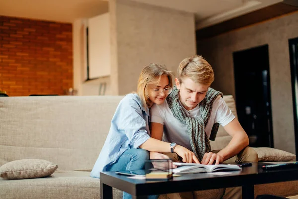 Pareja de estudiantes que estudian, libro de lectura mientras están sentados en el sofá — Foto de Stock